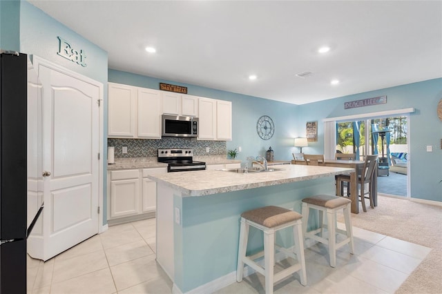 kitchen with a kitchen island with sink, light carpet, sink, white cabinetry, and stainless steel appliances