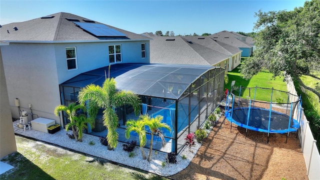 back of house featuring glass enclosure, a yard, and a trampoline