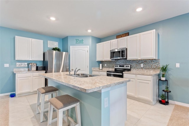 kitchen with a kitchen bar, stainless steel appliances, sink, white cabinetry, and an island with sink