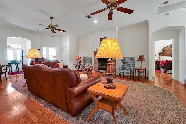 living room with a brick fireplace, ceiling fan, ornamental molding, and hardwood / wood-style flooring