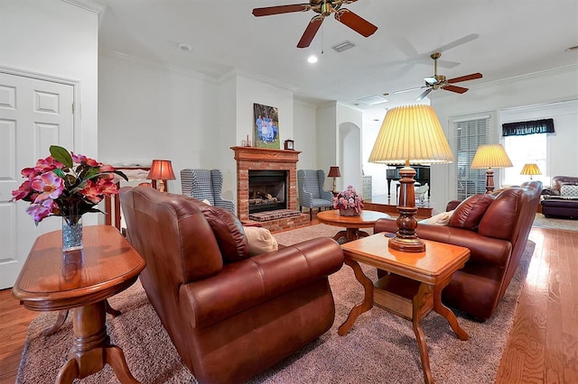 living room featuring hardwood / wood-style flooring, ornamental molding, a brick fireplace, and ceiling fan