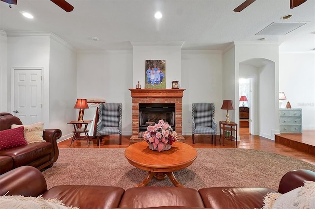 living room featuring a fireplace, ceiling fan, crown molding, hardwood / wood-style floors, and a textured ceiling