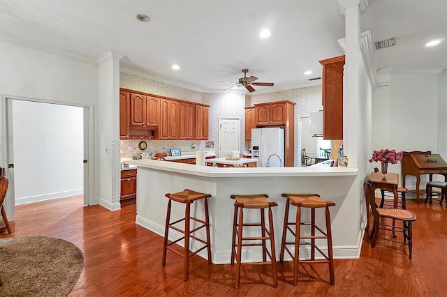 kitchen featuring a kitchen breakfast bar, ornamental molding, hardwood / wood-style flooring, ceiling fan, and white refrigerator with ice dispenser