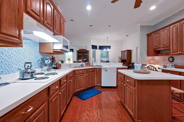 kitchen featuring kitchen peninsula, ceiling fan with notable chandelier, hardwood / wood-style flooring, a kitchen bar, and white appliances