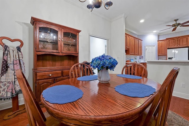 dining space featuring ornamental molding, wood-type flooring, and ceiling fan with notable chandelier