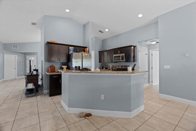 kitchen with dark brown cabinetry, light tile flooring, stainless steel appliances, vaulted ceiling, and light stone countertops