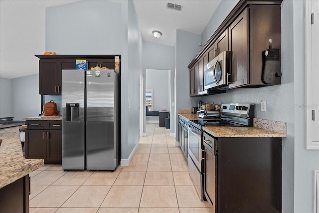 kitchen featuring dark brown cabinetry, stainless steel appliances, light stone countertops, and light tile floors