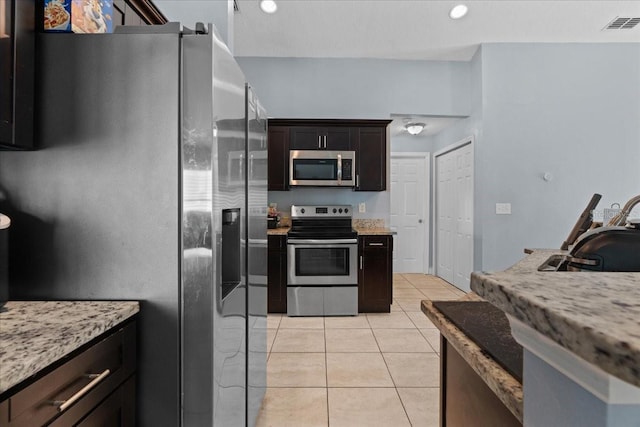 kitchen with dark brown cabinets, stainless steel appliances, light stone countertops, and light tile floors