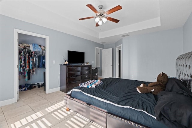 tiled bedroom with a walk in closet, ceiling fan, a raised ceiling, and a closet