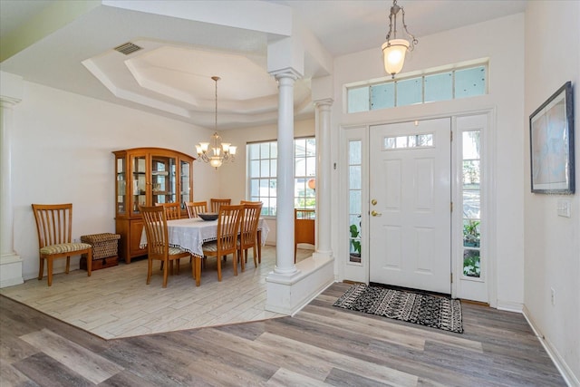 entryway with a tray ceiling, decorative columns, and a notable chandelier