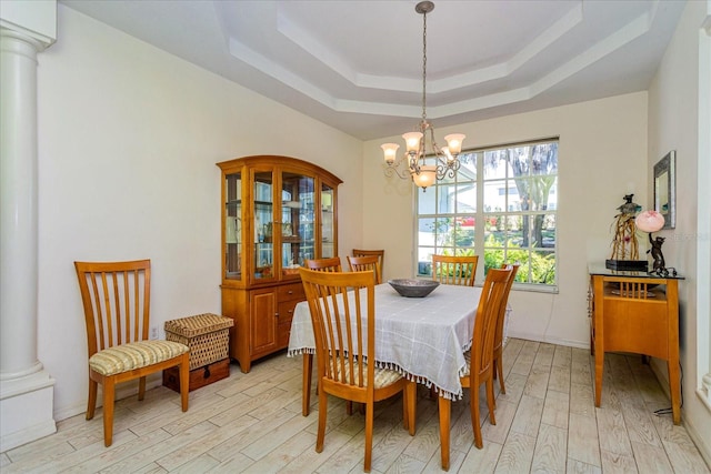 dining space with an inviting chandelier, light wood-type flooring, a raised ceiling, and ornate columns