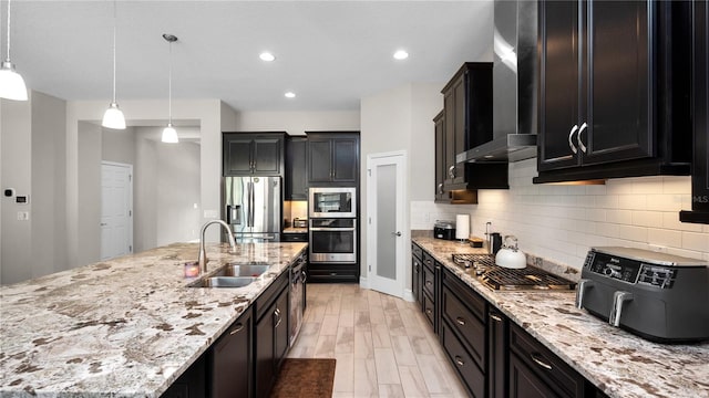 kitchen with light stone countertops, sink, wall chimney exhaust hood, pendant lighting, and appliances with stainless steel finishes