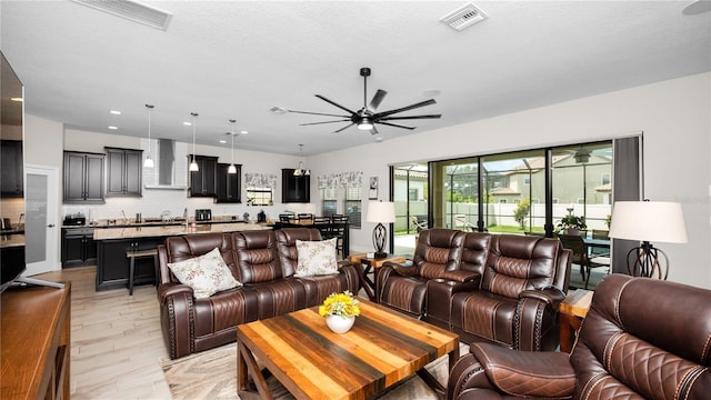 living room featuring ceiling fan, light wood-type flooring, and a textured ceiling