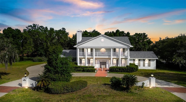 neoclassical / greek revival house featuring a balcony, covered porch, and a lawn