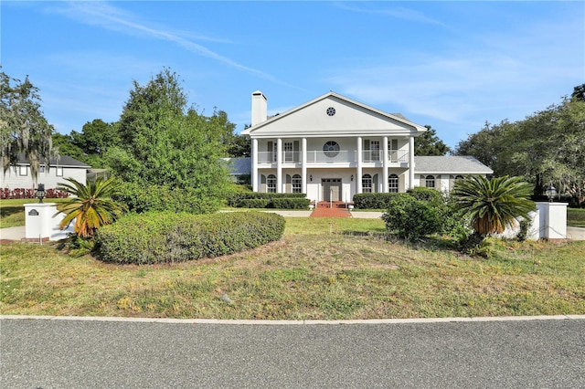 neoclassical / greek revival house with a balcony, french doors, and a front lawn