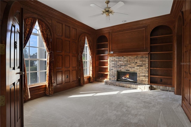 unfurnished living room with built in shelves, light colored carpet, ceiling fan, and a fireplace