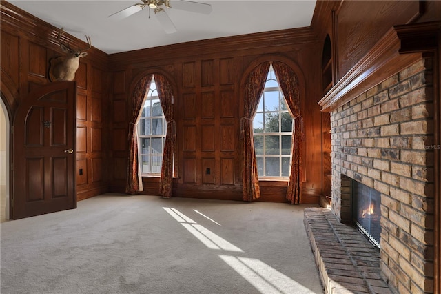 unfurnished living room featuring a fireplace, wood walls, ceiling fan, and carpet flooring