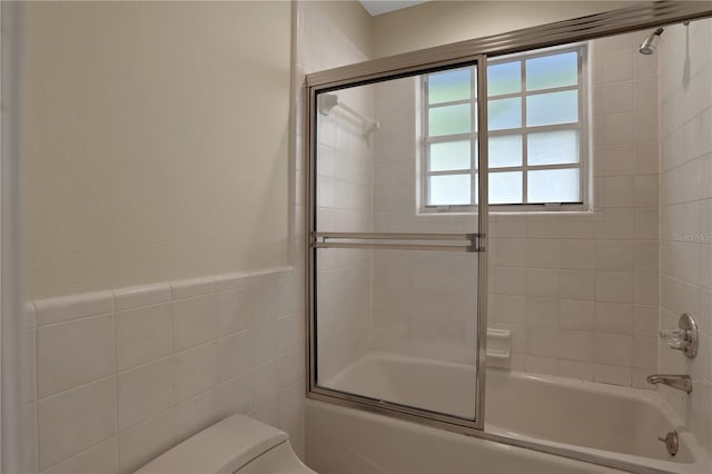 bathroom featuring tile walls, shower / bath combination with glass door, and toilet