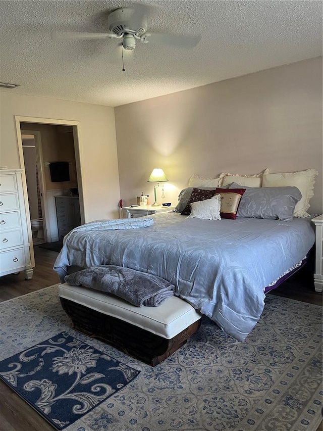 bedroom with ceiling fan, dark hardwood / wood-style flooring, a textured ceiling, and connected bathroom