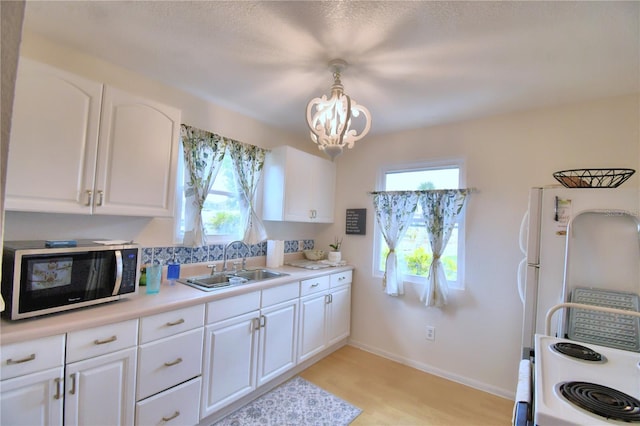 kitchen with decorative light fixtures, light wood-type flooring, white cabinetry, a notable chandelier, and sink