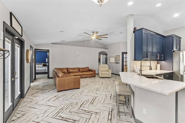 kitchen featuring arched walkways, light countertops, vaulted ceiling, and a sink