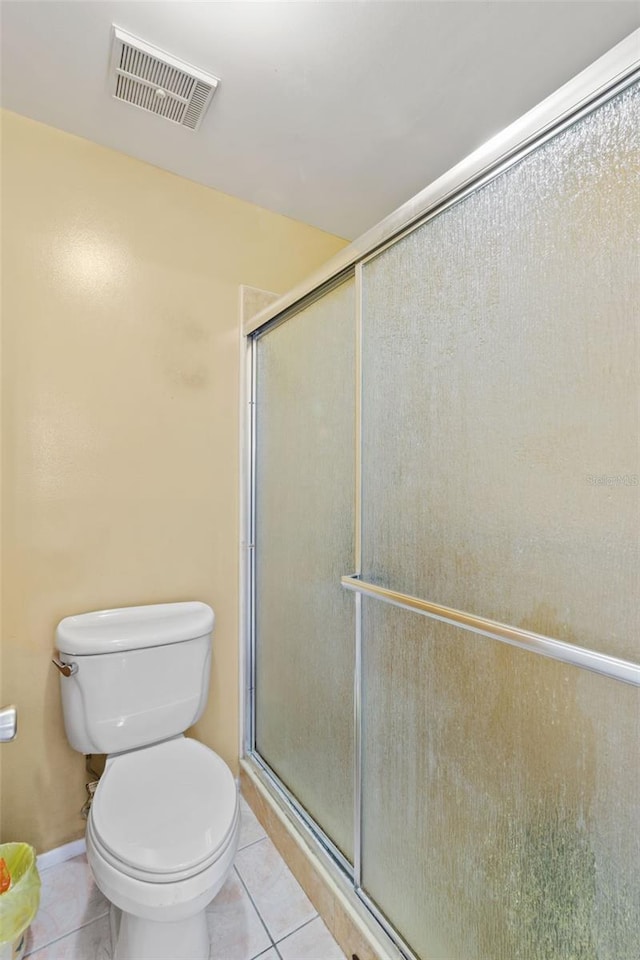 bathroom with tile floors, toilet, and a shower with shower door