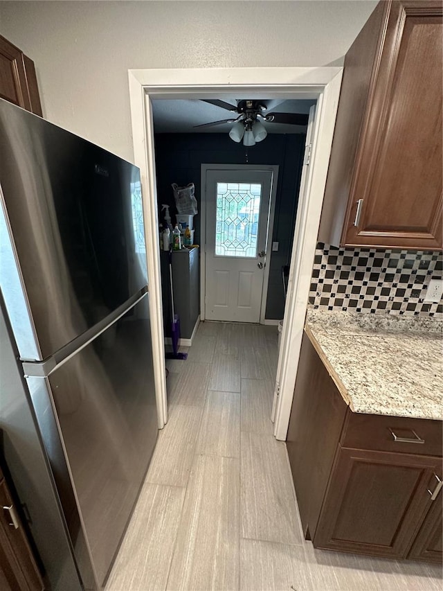 kitchen featuring dark brown cabinetry, ceiling fan, tasteful backsplash, light stone countertops, and stainless steel fridge