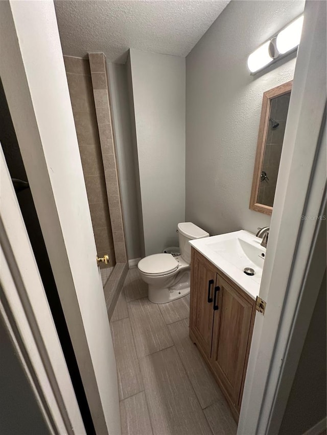 bathroom featuring a shower, a textured ceiling, large vanity, and toilet