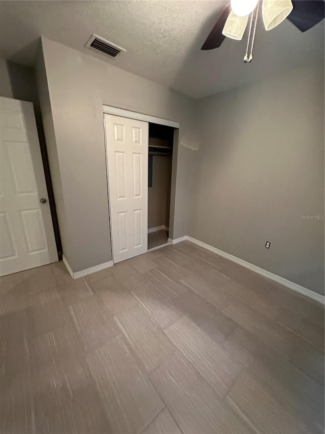 unfurnished bedroom with a textured ceiling, a closet, wood-type flooring, and ceiling fan