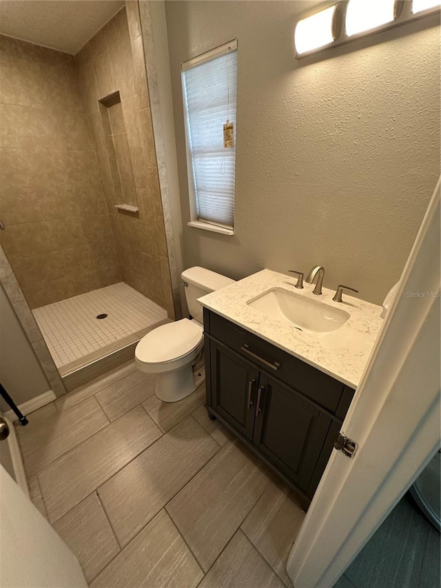 bathroom with tiled shower, vanity, toilet, and tile floors