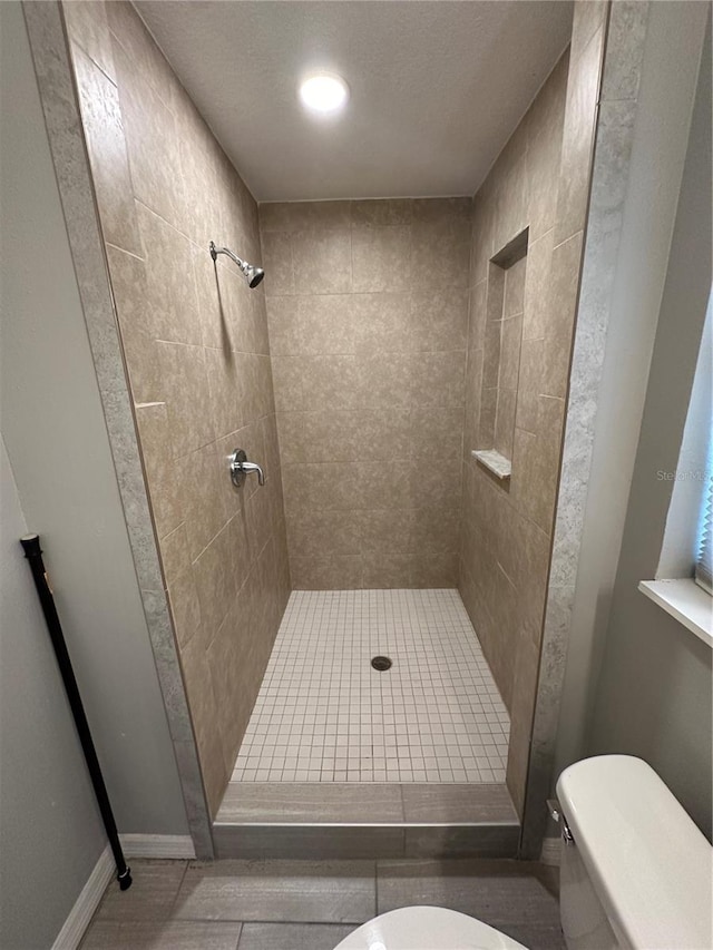 bathroom with tiled shower, tile floors, and toilet