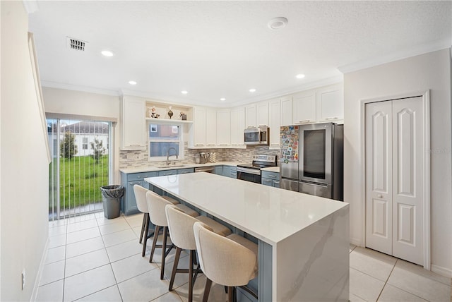 kitchen featuring light tile patterned flooring, white cabinets, appliances with stainless steel finishes, a kitchen island, and a breakfast bar area