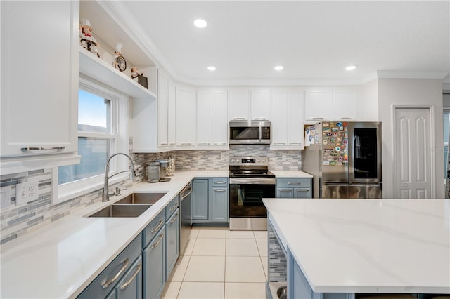 kitchen with appliances with stainless steel finishes, ornamental molding, sink, light tile patterned floors, and white cabinetry