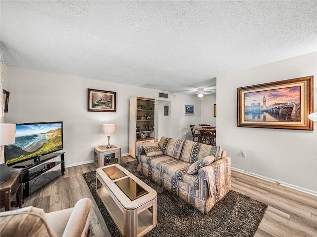 living room featuring ceiling fan, a textured ceiling, and wood-type flooring