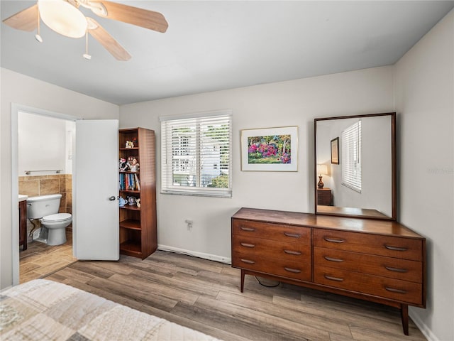 bedroom with ensuite bath, ceiling fan, tile walls, and hardwood / wood-style flooring