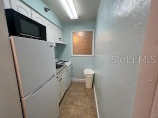 kitchen featuring white appliances, white cabinets, and light tile floors