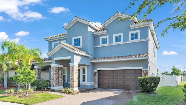 mediterranean / spanish home with stucco siding, an attached garage, decorative driveway, and fence