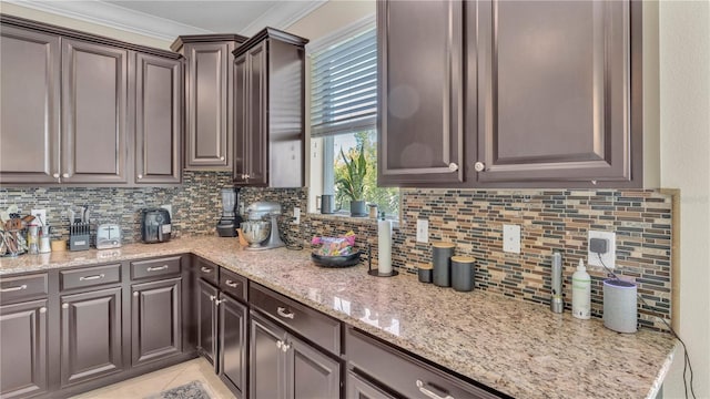 kitchen featuring dark brown cabinetry, decorative backsplash, light stone countertops, light tile patterned floors, and crown molding