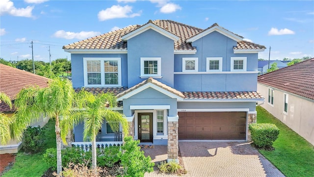 mediterranean / spanish-style home with stucco siding, a tiled roof, an attached garage, and decorative driveway