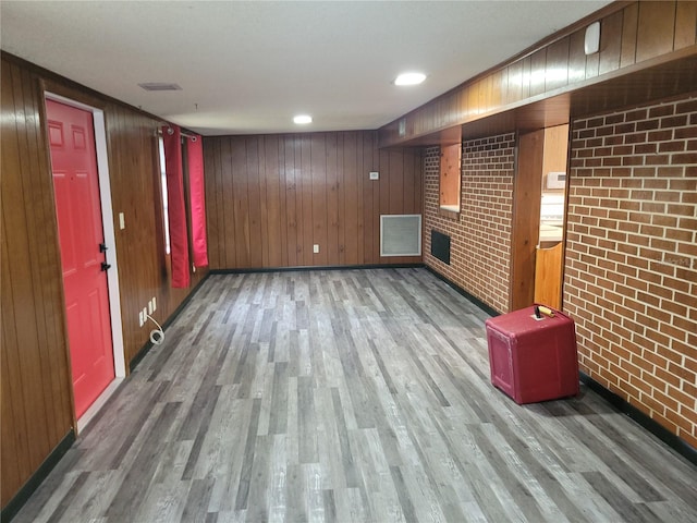 basement featuring wooden walls, brick wall, and wood-type flooring