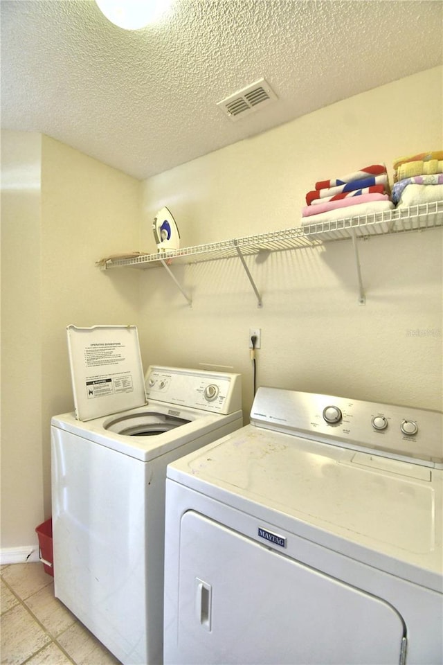 clothes washing area featuring separate washer and dryer, a textured ceiling, and light tile patterned floors