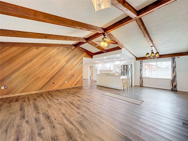 unfurnished living room featuring ceiling fan with notable chandelier, wood-type flooring, a textured ceiling, and wooden walls