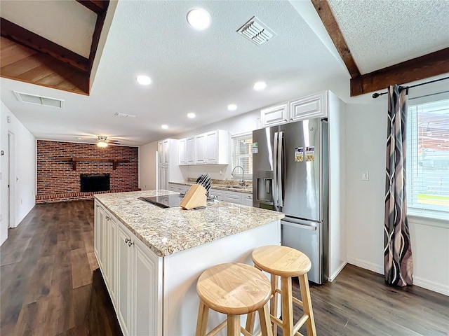 kitchen with white cabinetry, a center island, a brick fireplace, brick wall, and stainless steel fridge