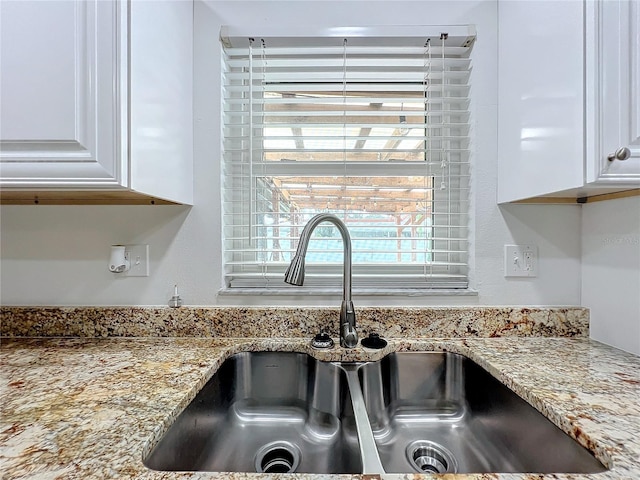 room details featuring white cabinets, light stone counters, and sink