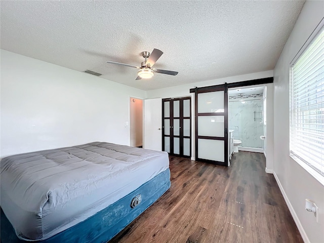 bedroom with a textured ceiling, dark hardwood / wood-style floors, ceiling fan, and connected bathroom