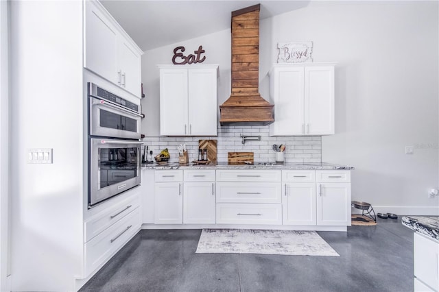 kitchen with lofted ceiling, premium range hood, double oven, light stone countertops, and white cabinets