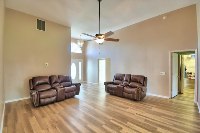 living area featuring light wood finished floors, baseboards, visible vents, a ceiling fan, and a towering ceiling