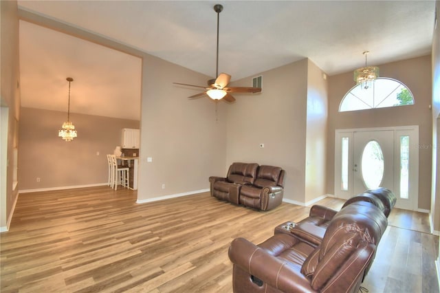 living area featuring light wood finished floors, a high ceiling, baseboards, and ceiling fan with notable chandelier