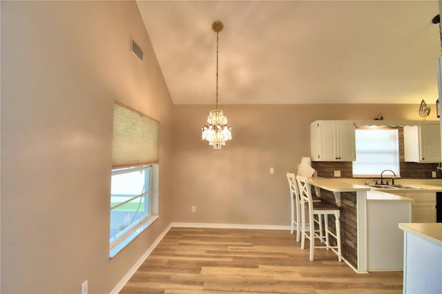 kitchen with lofted ceiling, visible vents, white cabinets, hanging light fixtures, and light countertops