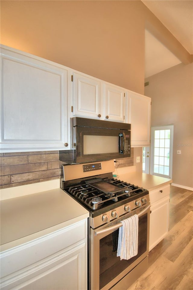 kitchen featuring black microwave, white cabinets, light countertops, stainless steel gas range, and light wood-type flooring